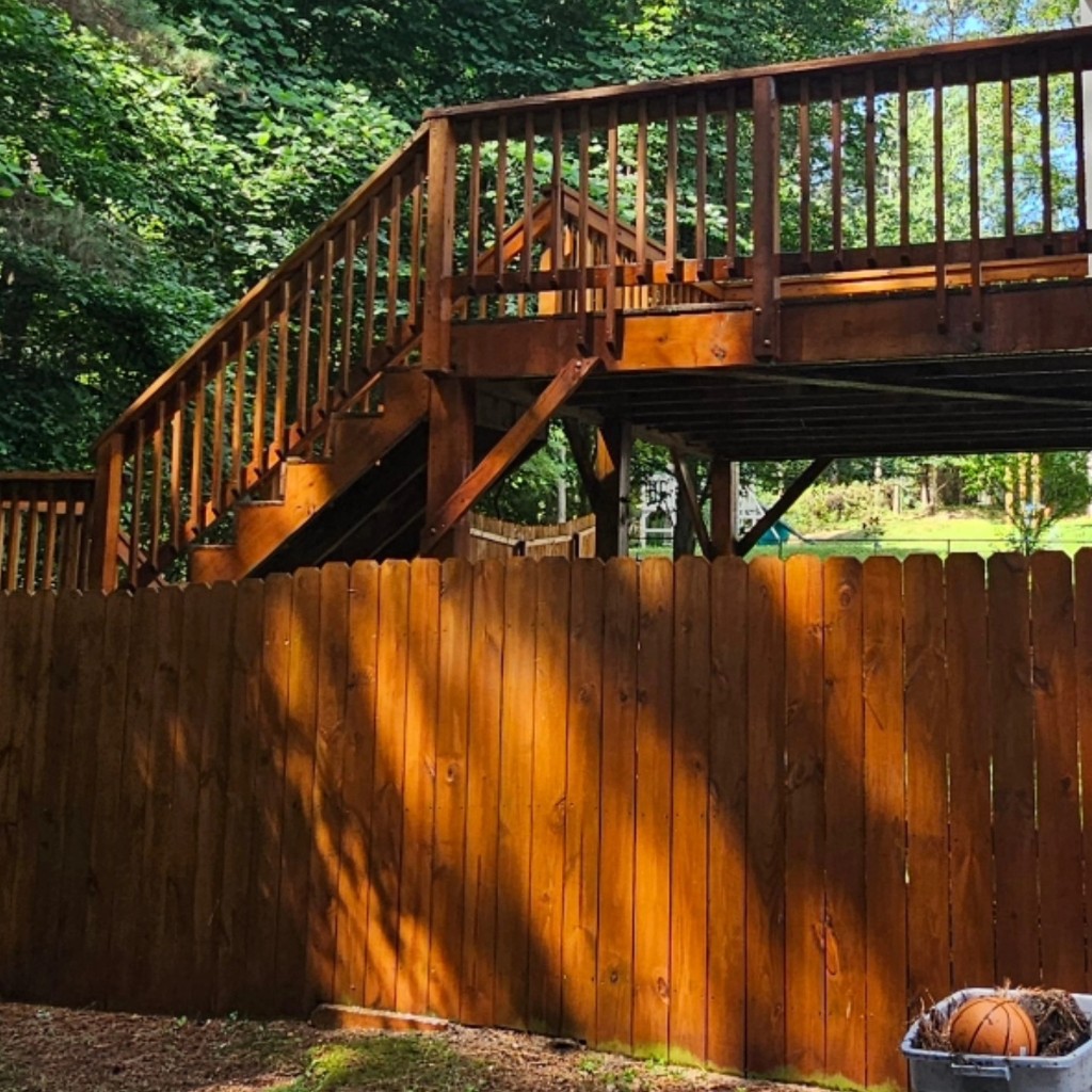 Clean stained wooden deck with stairs and privacy fence in a backyard
