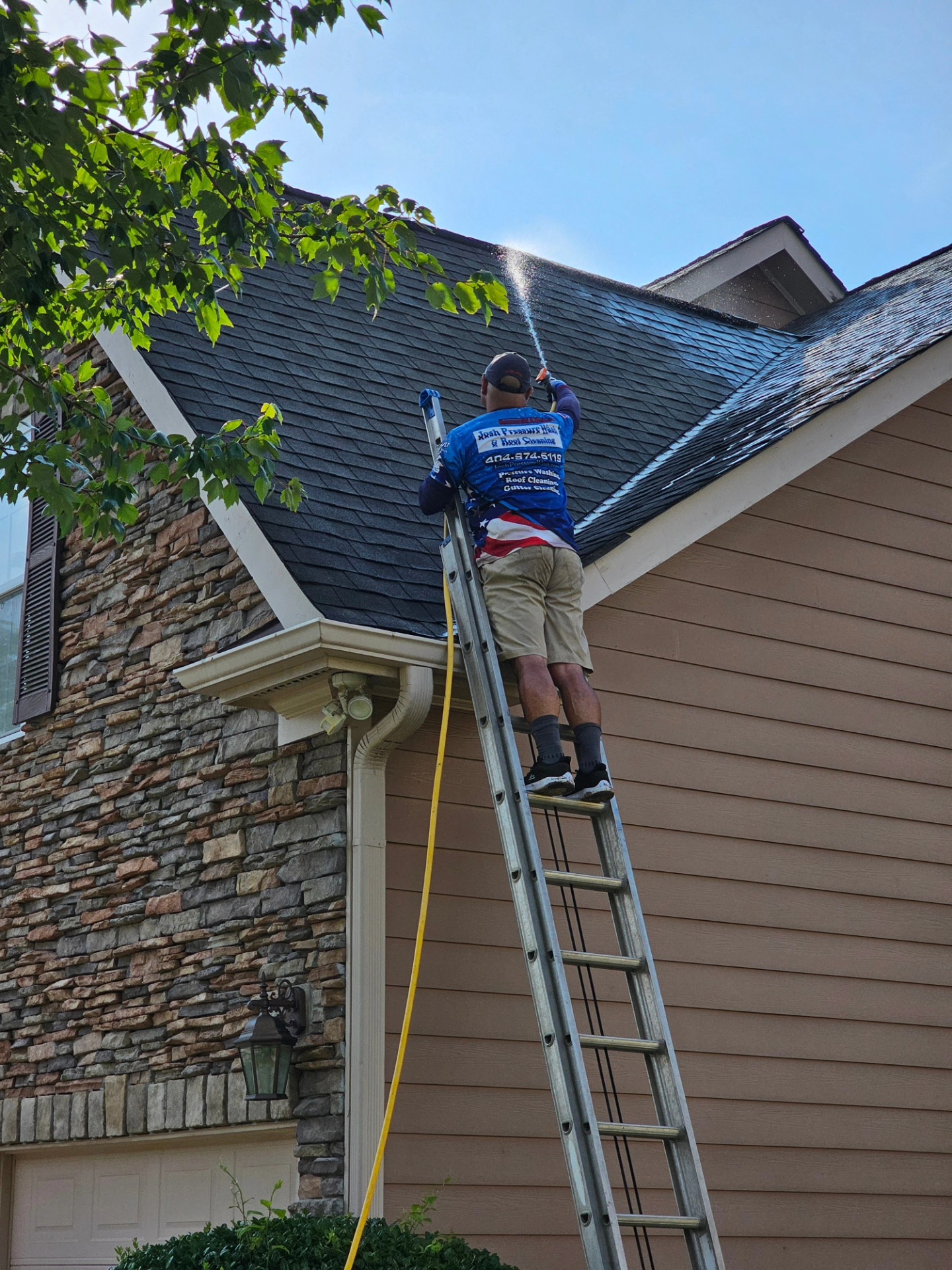 Technician on a ladder soft washing a shingle roof